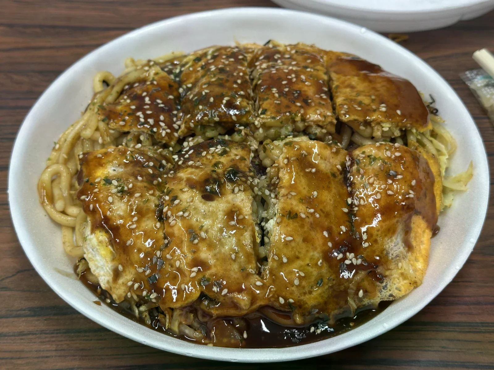 烏龍麵從廣島風御好燒的邊緣露出，表面淋有醬汁並撒上芝麻