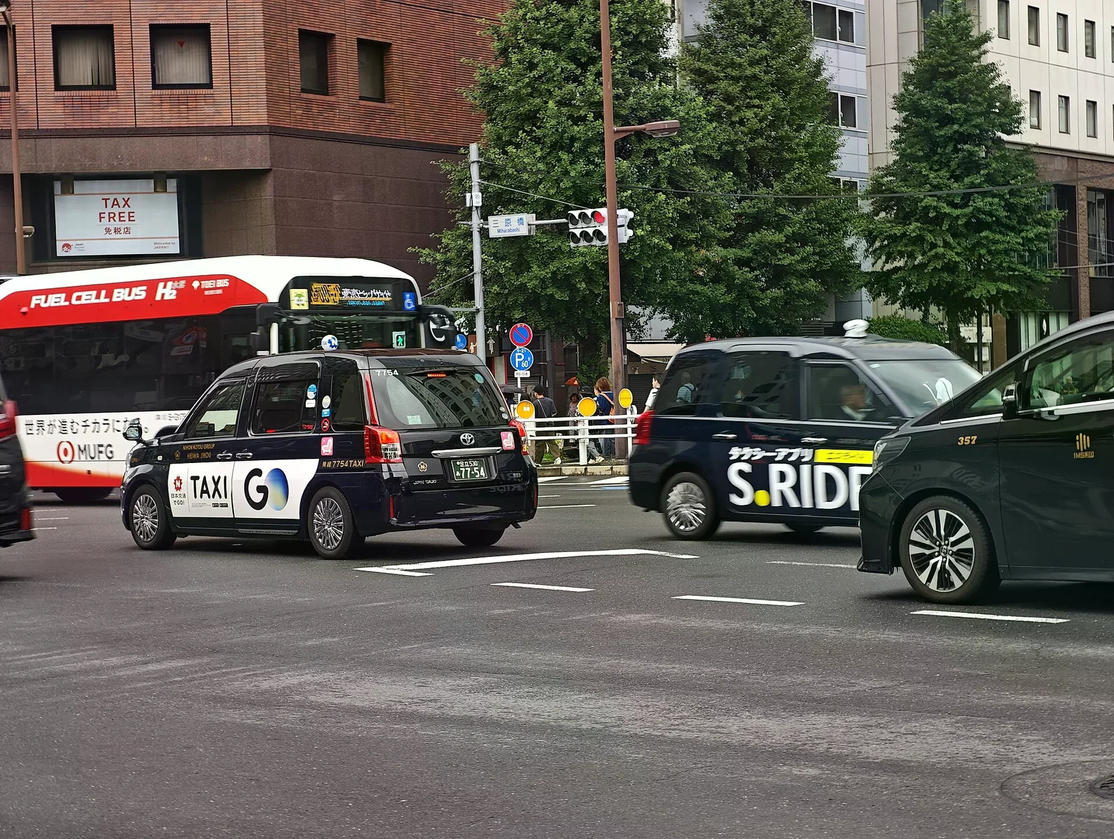銀座五丁目三原橋交叉口路上數輛計程車流動，車身帶動態模糊，街道兩側是都市建築。