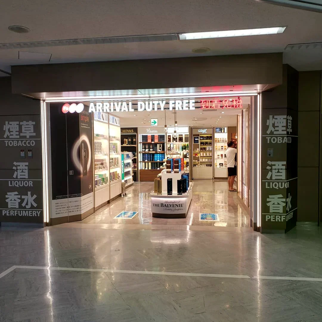 機場入境大廳的到著免稅店門口，門頭標示 ARRIVAL DUTY FREE，兩側牆面寫著菸草、酒、香水
