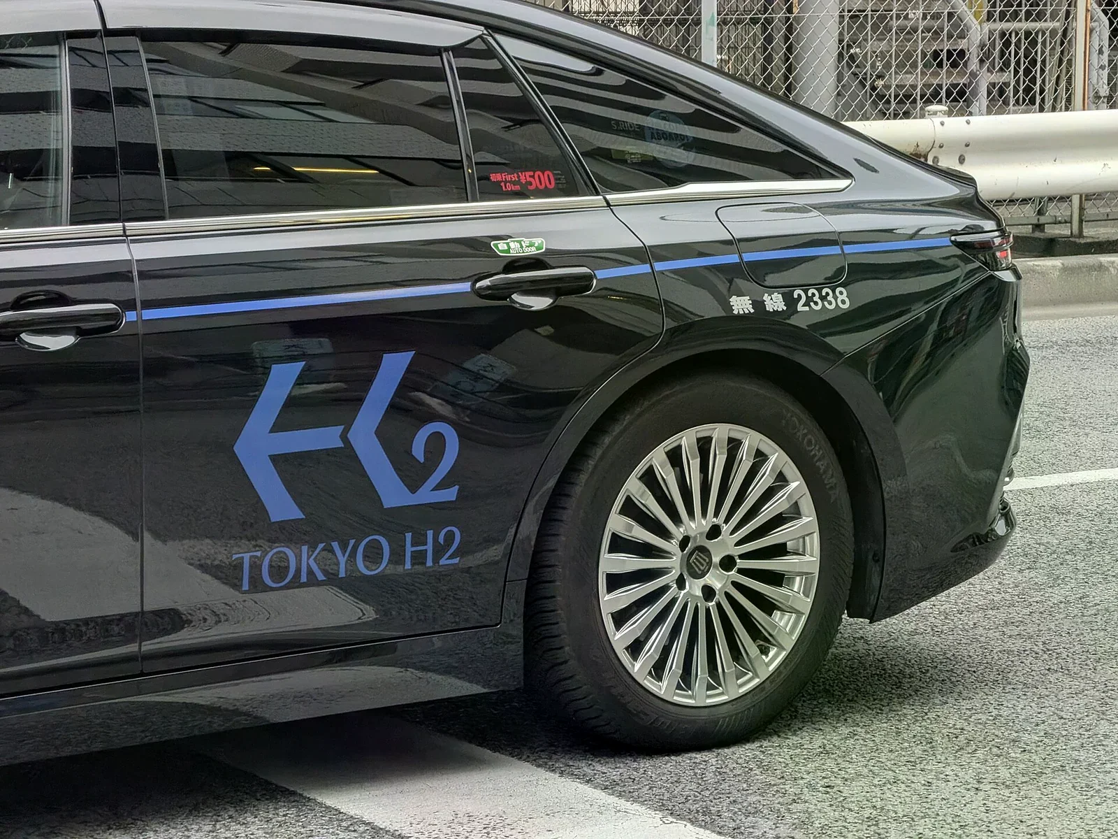 東京一輛黑色計程車的車身側邊，藍色 H2 字樣與無線 2338 編號，停在柏油路面上