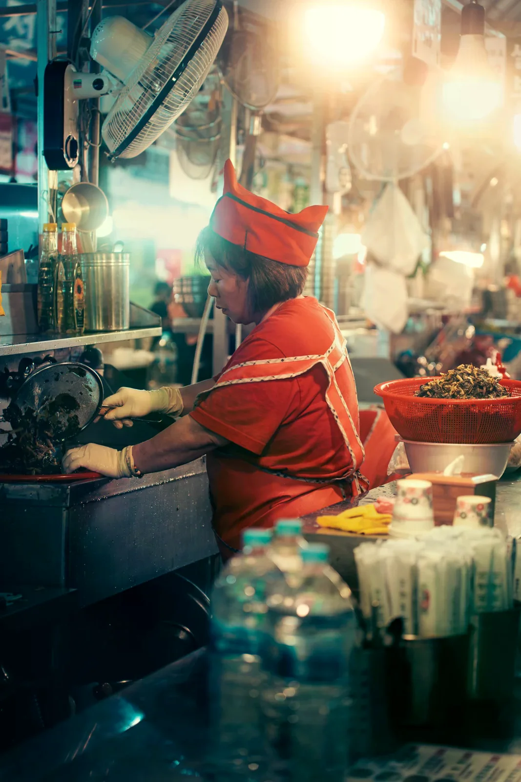 首爾市場廚房裡，一位穿紅衣的工作者在爐台旁準備食材