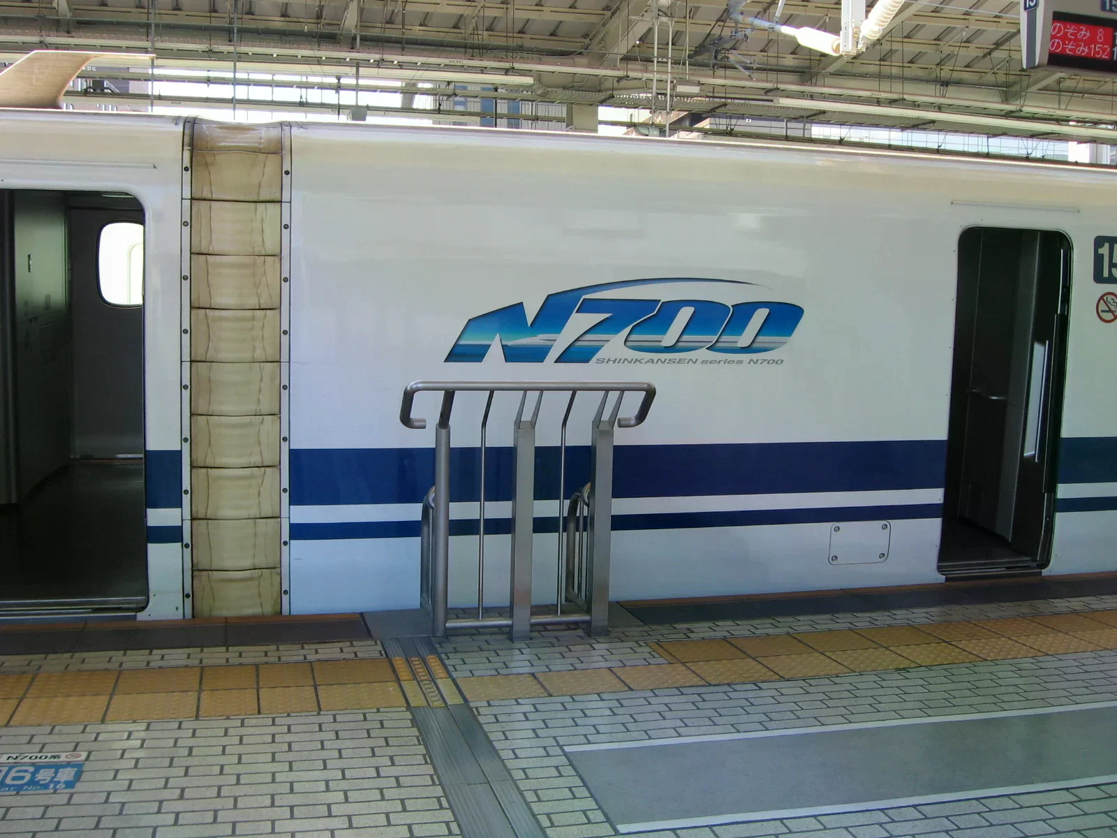東海道新幹線 N700 列車停靠月台，車身白藍雙色、車門開啟，站上電子看板寫著のぞみ班次