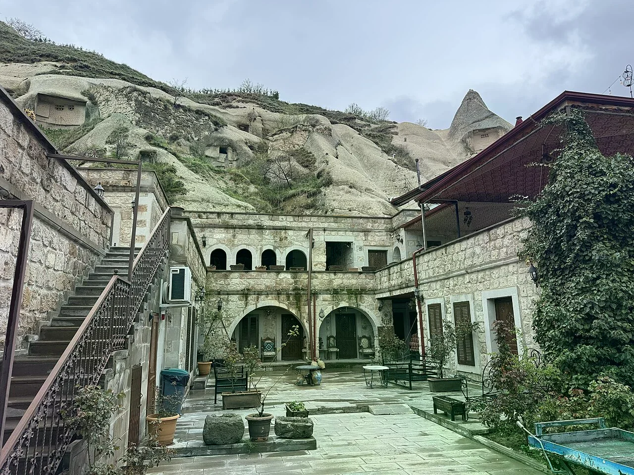 岩壁鑿建的洞穴飯店石砌中庭與拱廊，背靠火山岩坡，潮濕石板地面。