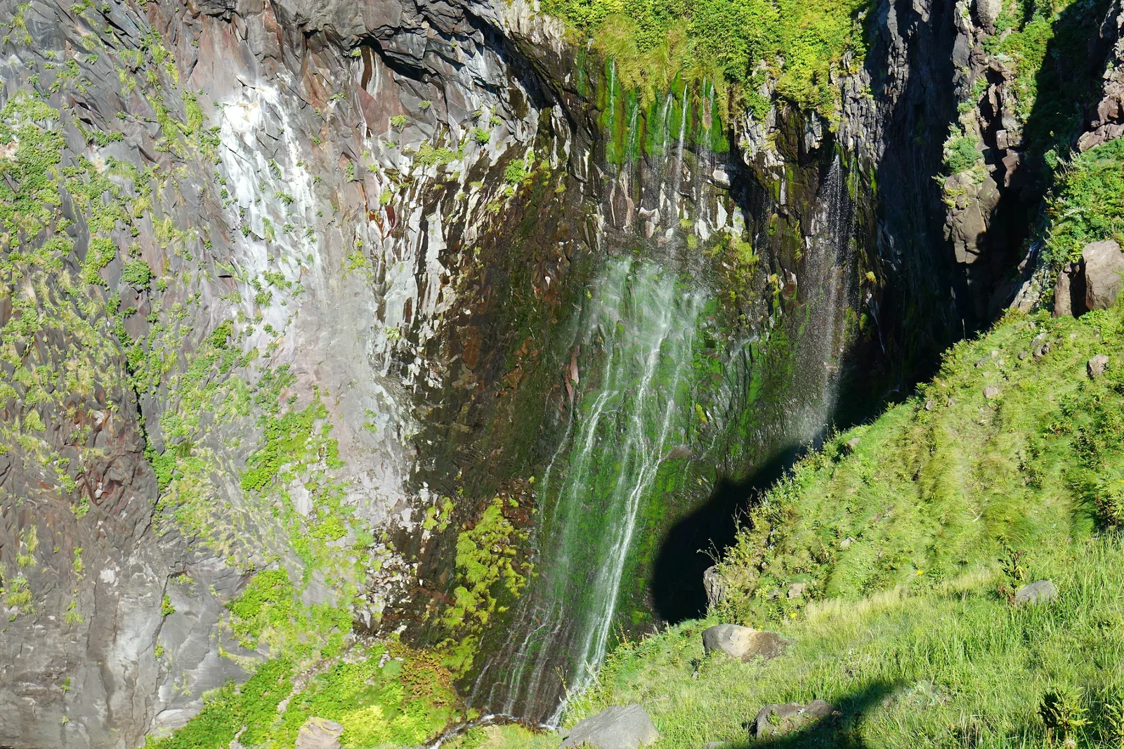 水流沿著陡峭海岸岩壁落向海面，周圍覆有綠色植被