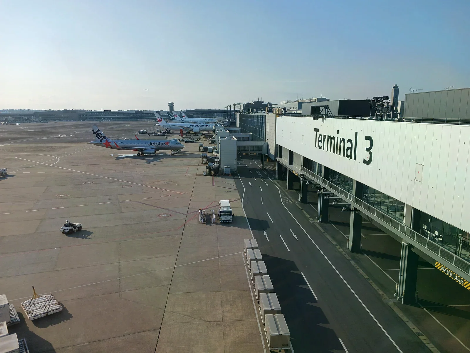 成田機場第三航廈空側，白色建築外牆寫著 Terminal 3，停機坪上有 Jetstar 與日本航空客機