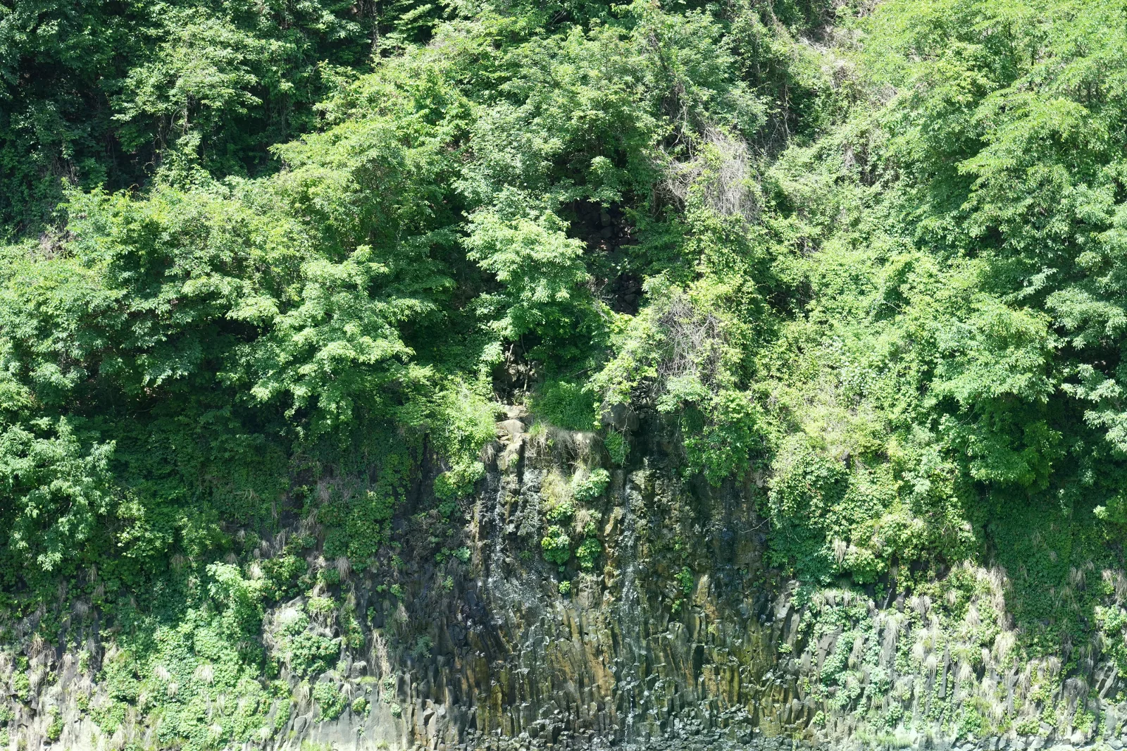 漢灘江河對岸的深色柱狀節理峭壁與河水，沒有棧道或遊客入鏡
