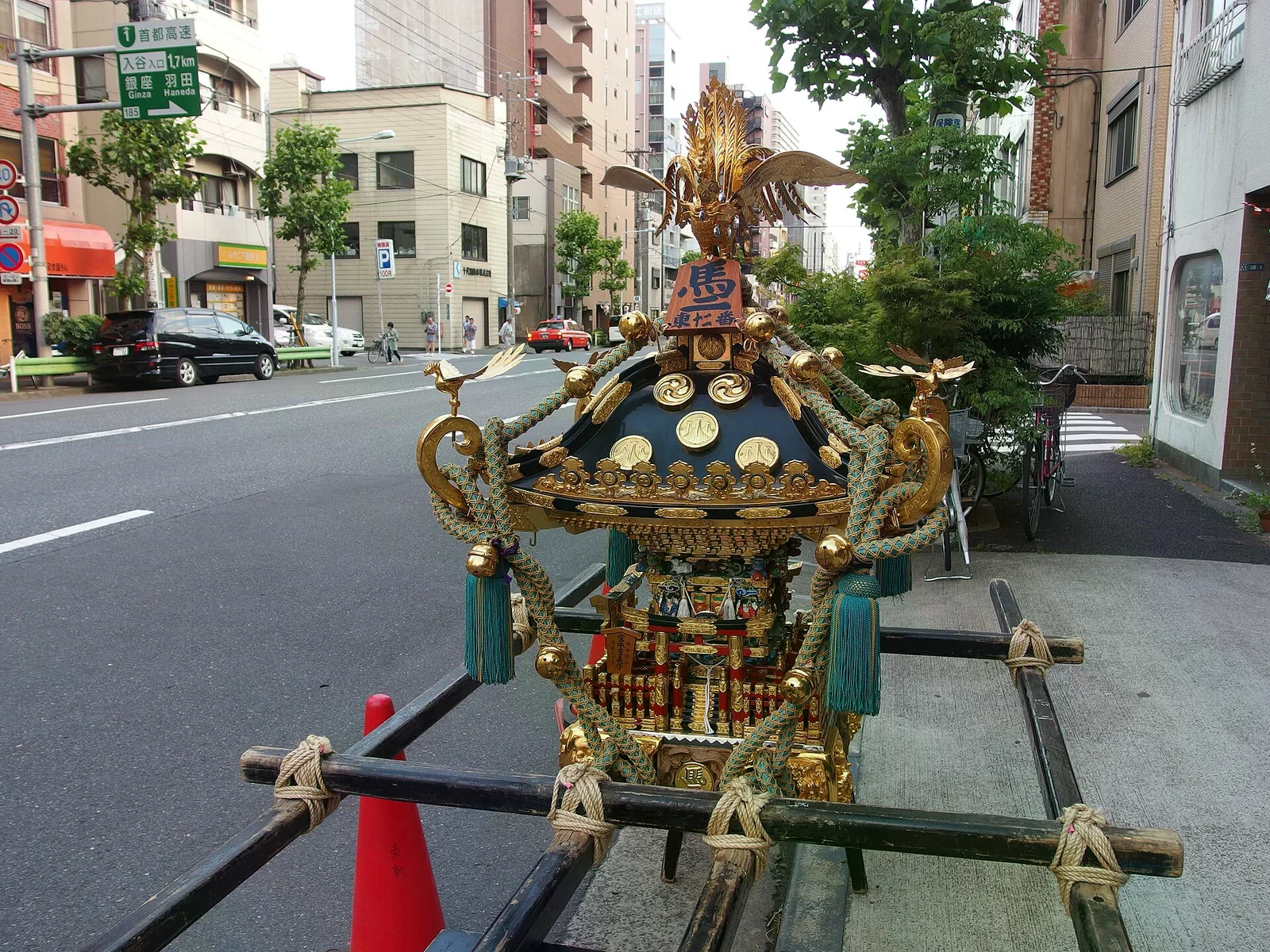一頂華麗的黑金配色神轎停在東京市區路旁，金色裝飾與抬轎木槓清晰可見，背景是街景