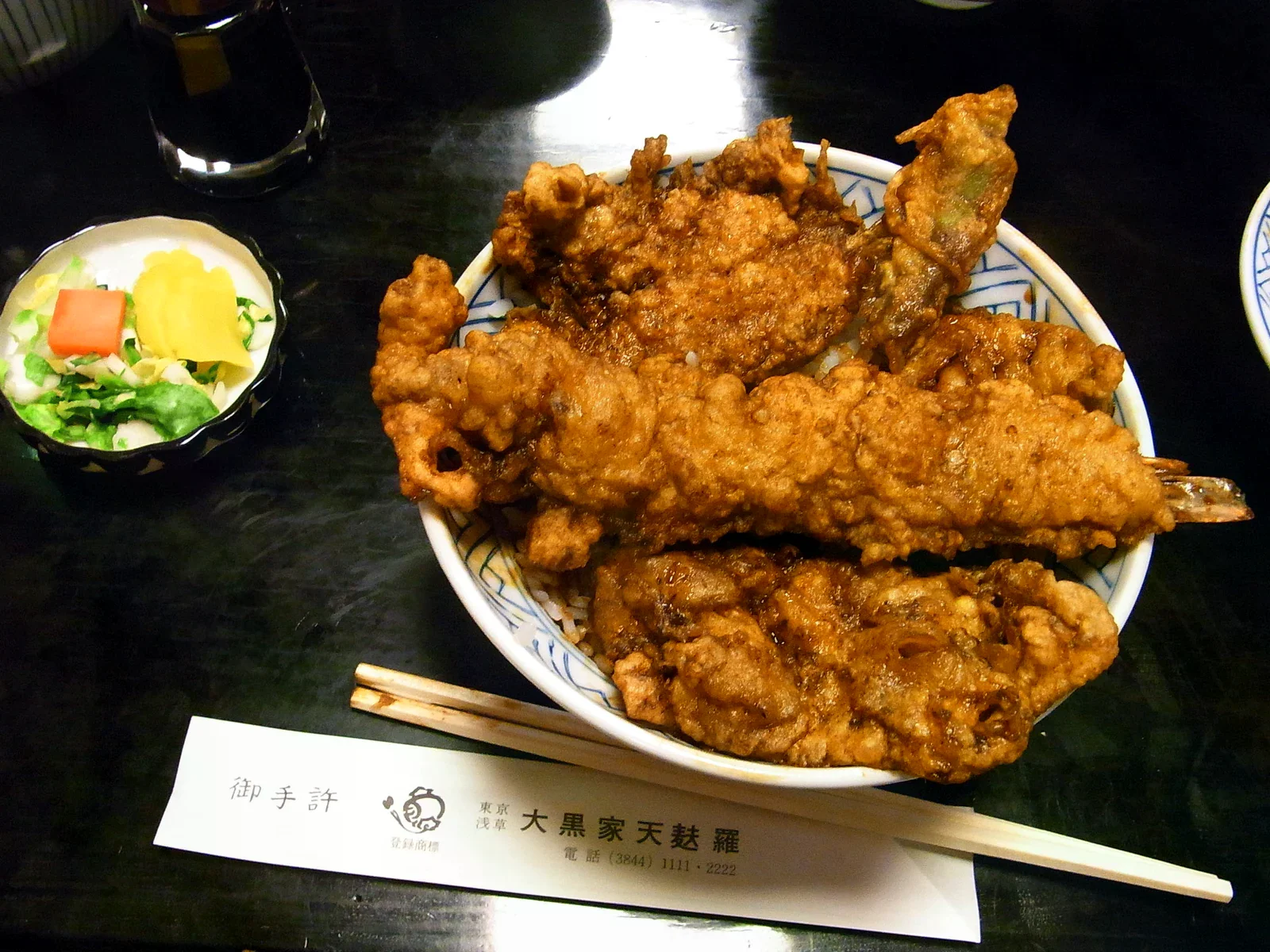 天丼上堆疊深色炸衣的天婦羅，旁有漬物