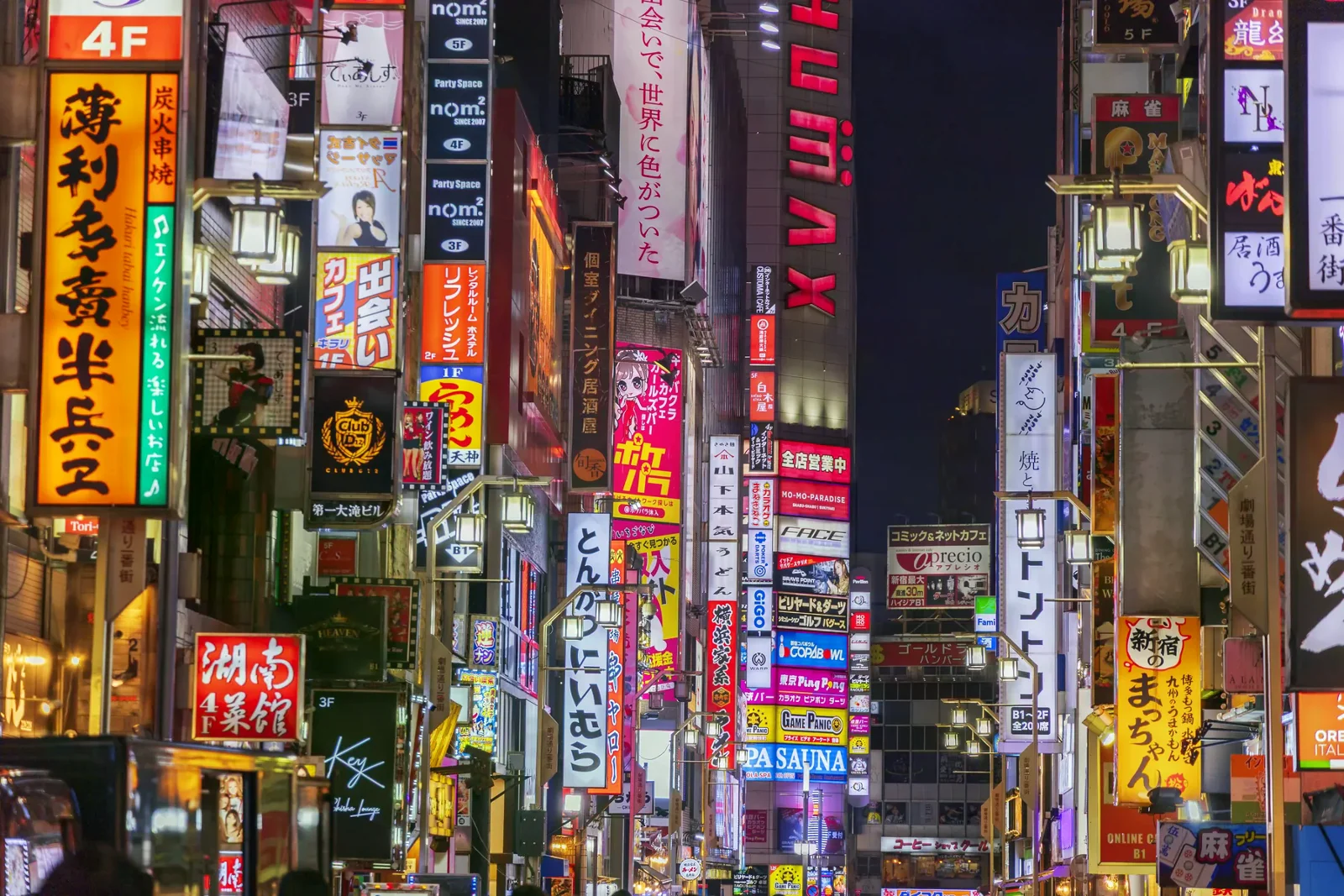 夜間霓虹照亮新宿街道，兩側可見多層店家招牌