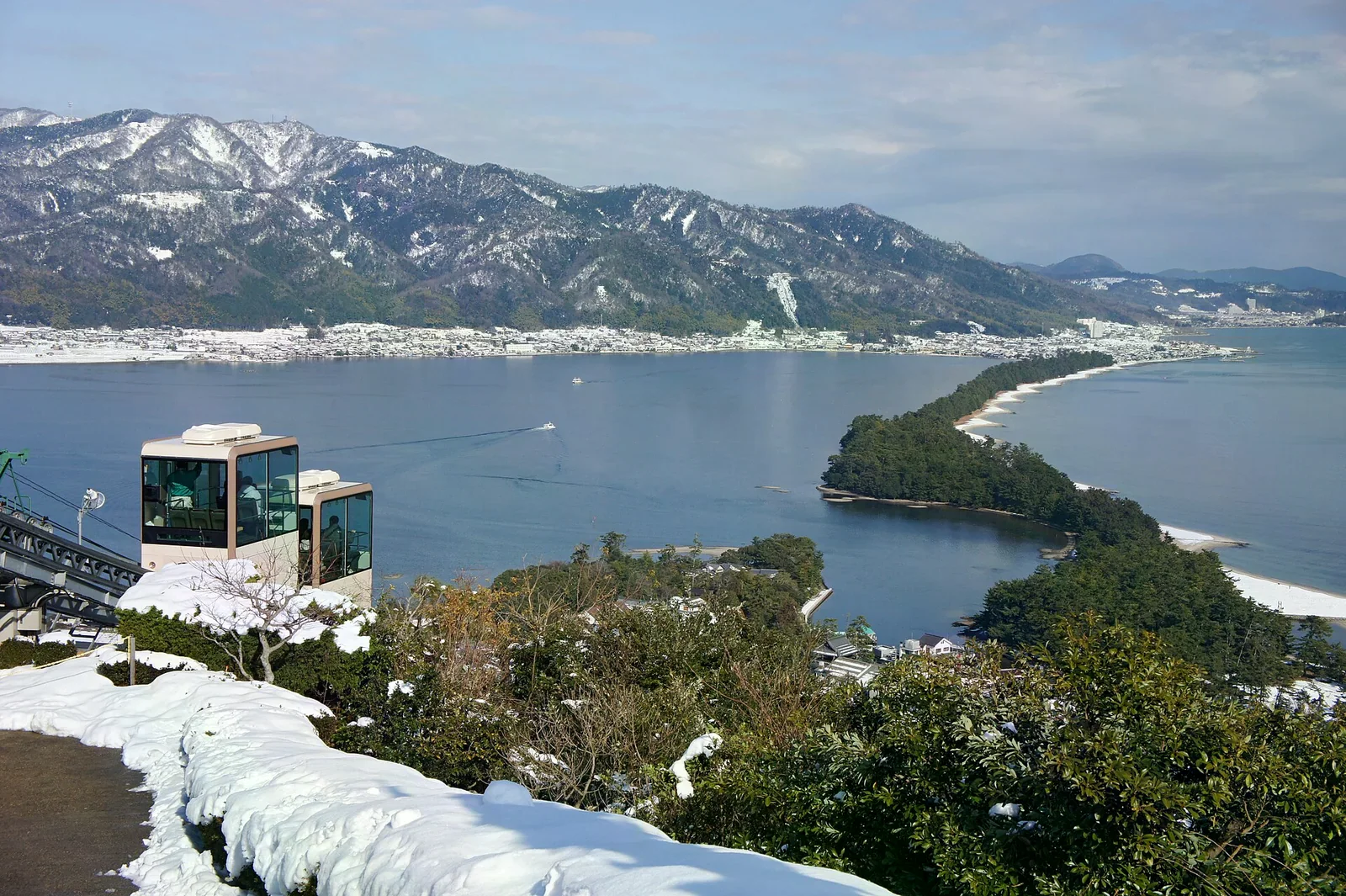 冬季畫面：View Land的單軌車貼山而行，前景地面與遠山有積雪，下方是彎向海灣的松帶沙洲