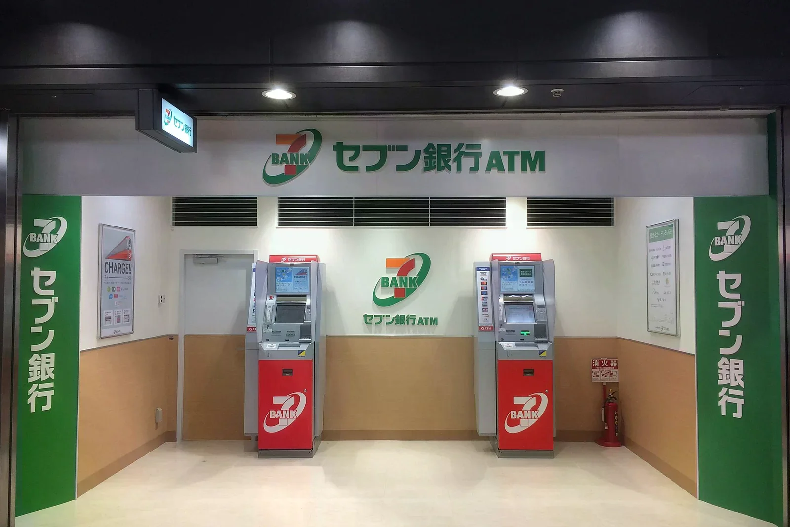 Seven Bank ATM 專區，兩台紅灰色提款機並排，牆上綠色 7-BANK 標誌與セブン銀行ATM 字樣
