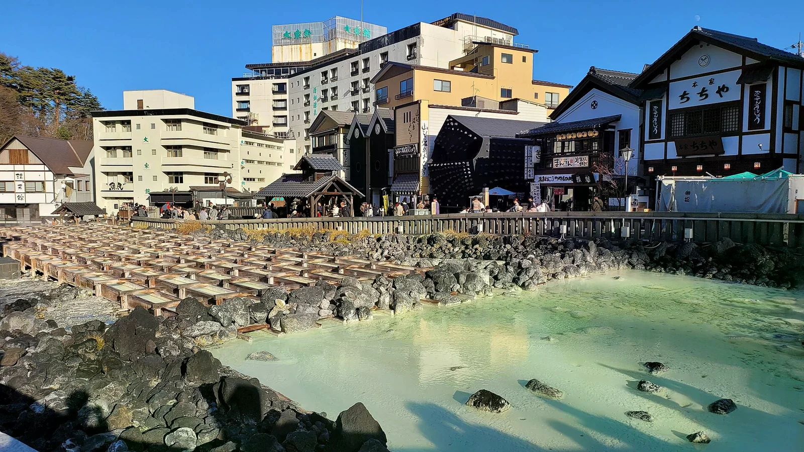 草津溫泉街頭乳白色湯畑，木格導流，旁邊是溫泉街屋與旅館