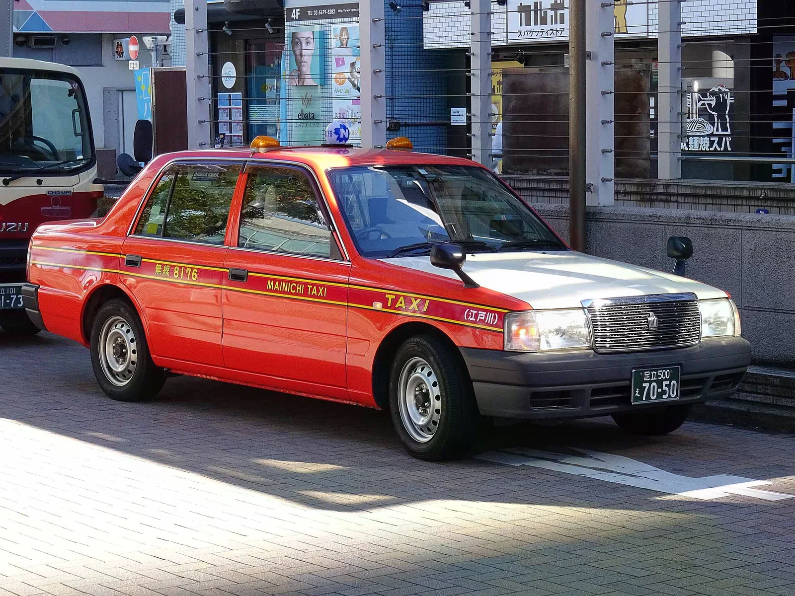 江戶川西葛西路邊一輛橘白配色 Crown Comfort 計程車停靠人行道旁，車身乾淨、車頂有計程車燈。