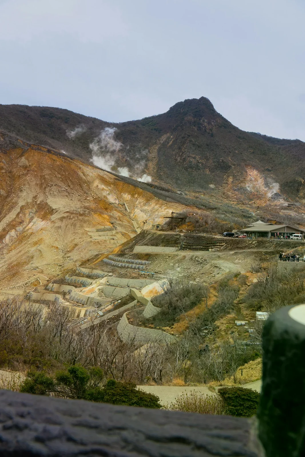 大涌谷裸露的火山地貌冒出白色蒸氣，遠處有設施建築