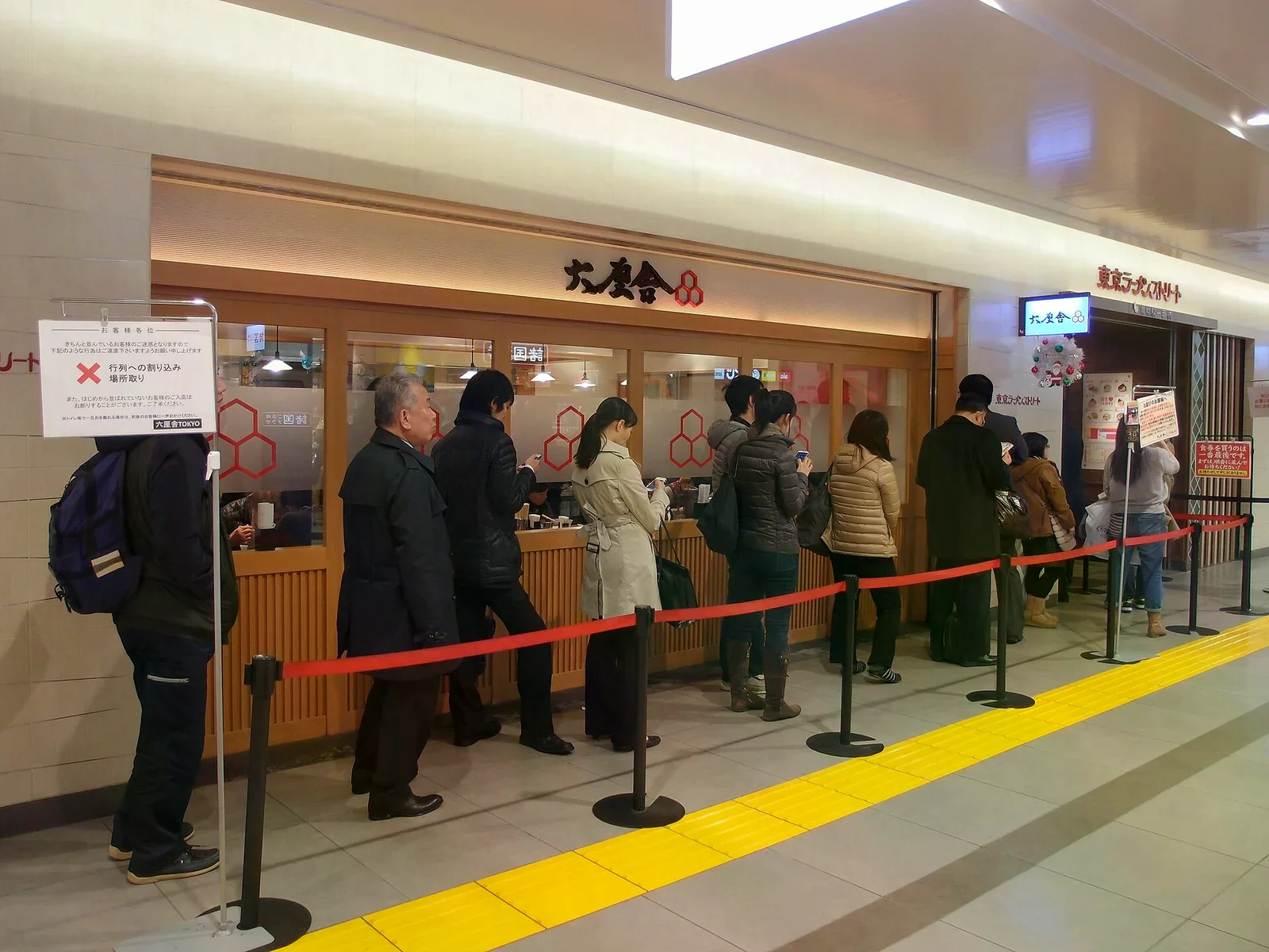 東京拉麵街的拉麵店前，紅色隔離帶圍出排隊動線，門口有六厘舍的招牌與注意事項立牌