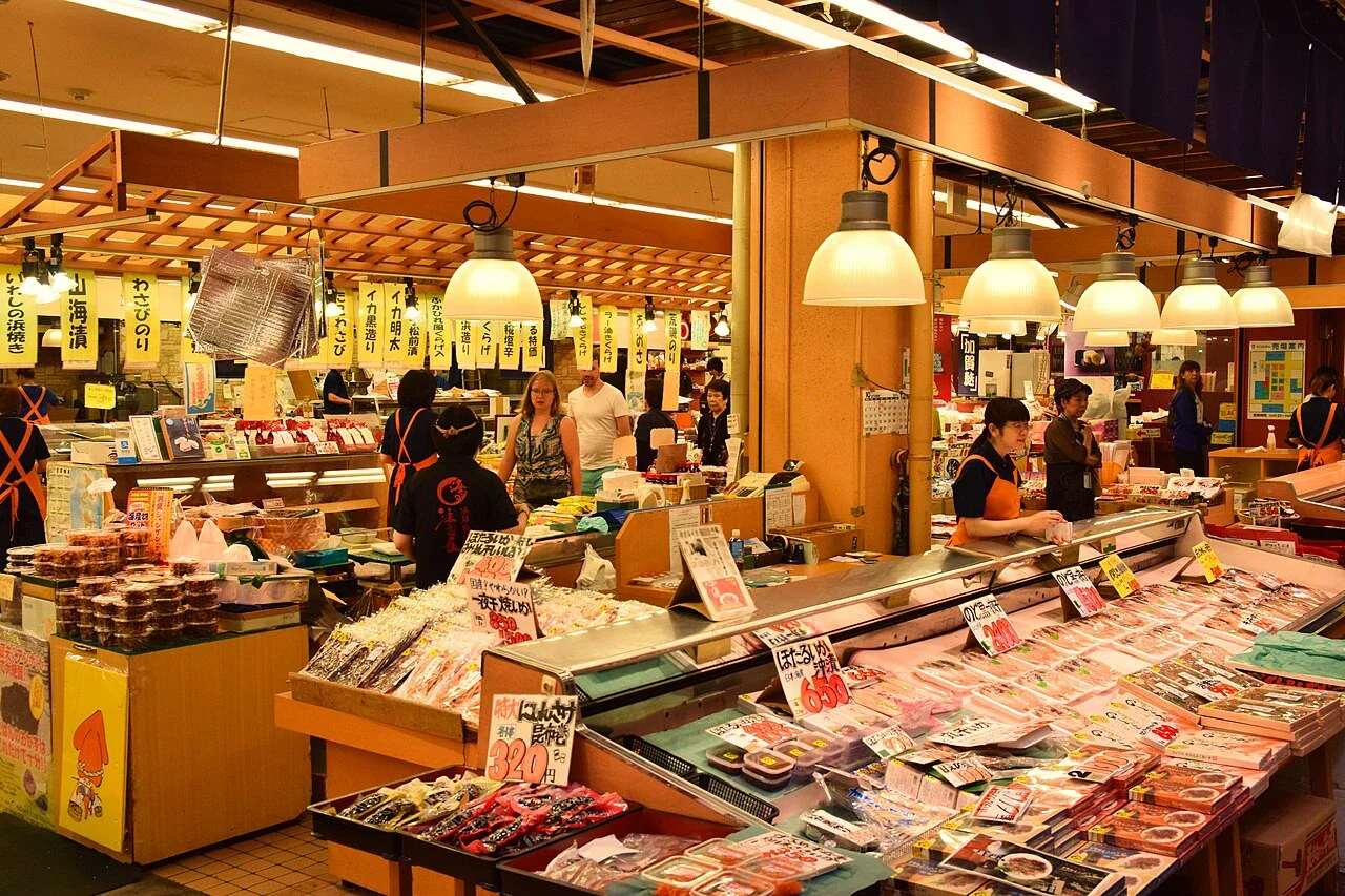 近江町市場室內鮮魚攤位與魚貨陳列，店員和顧客在攤位間活動