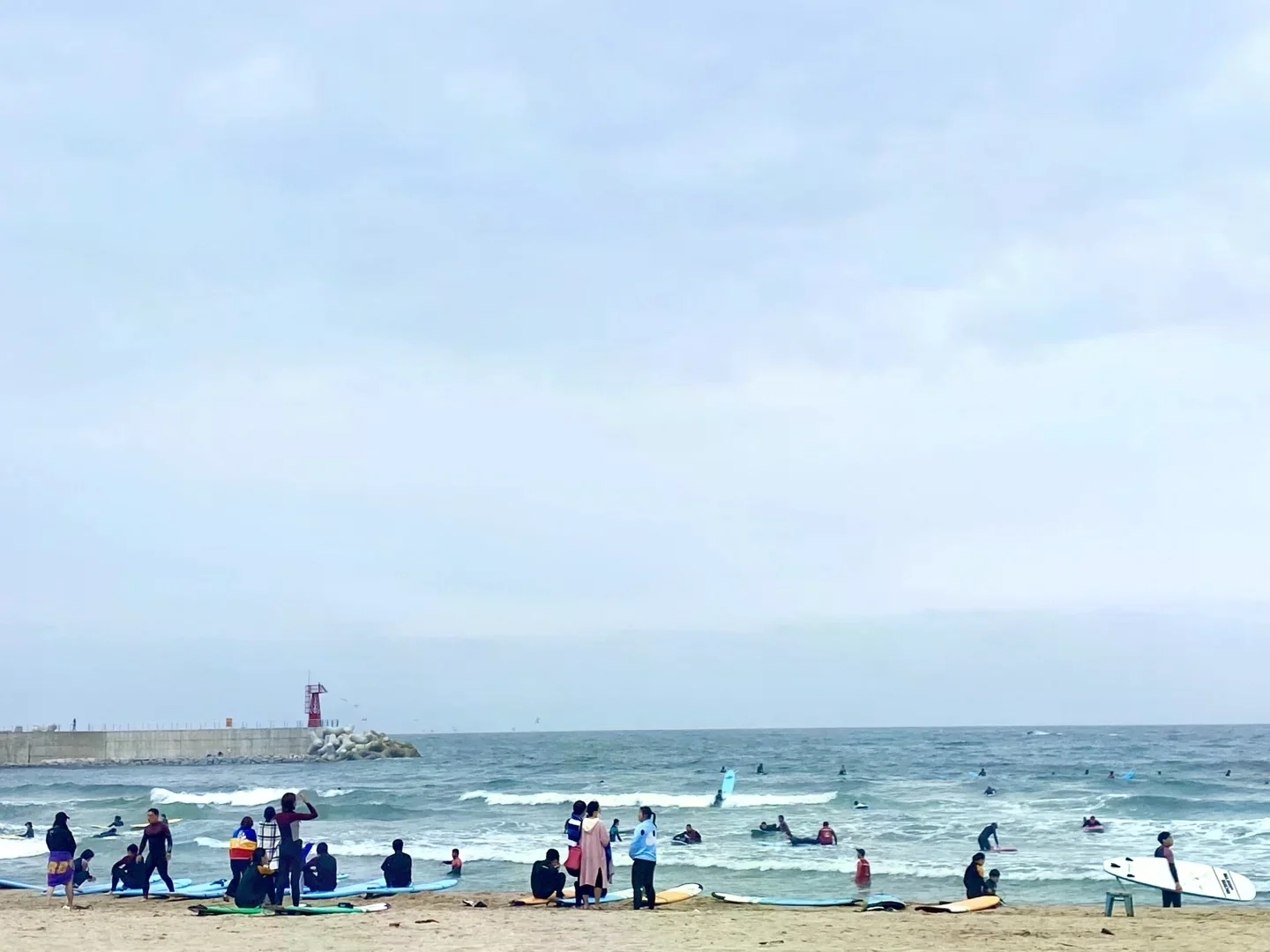 襄陽仁邱海邊有多位旅客和衝浪者在岸邊整理衝浪板、海面上有人練習