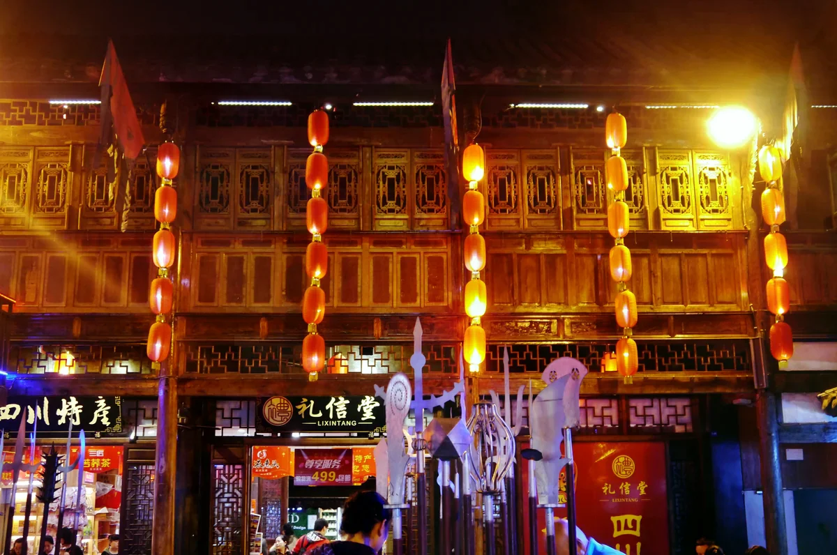 成都錦里古街夜景，傳統木結構二樓建築掛滿紅色燈籠，一樓是四川特產店鋪。