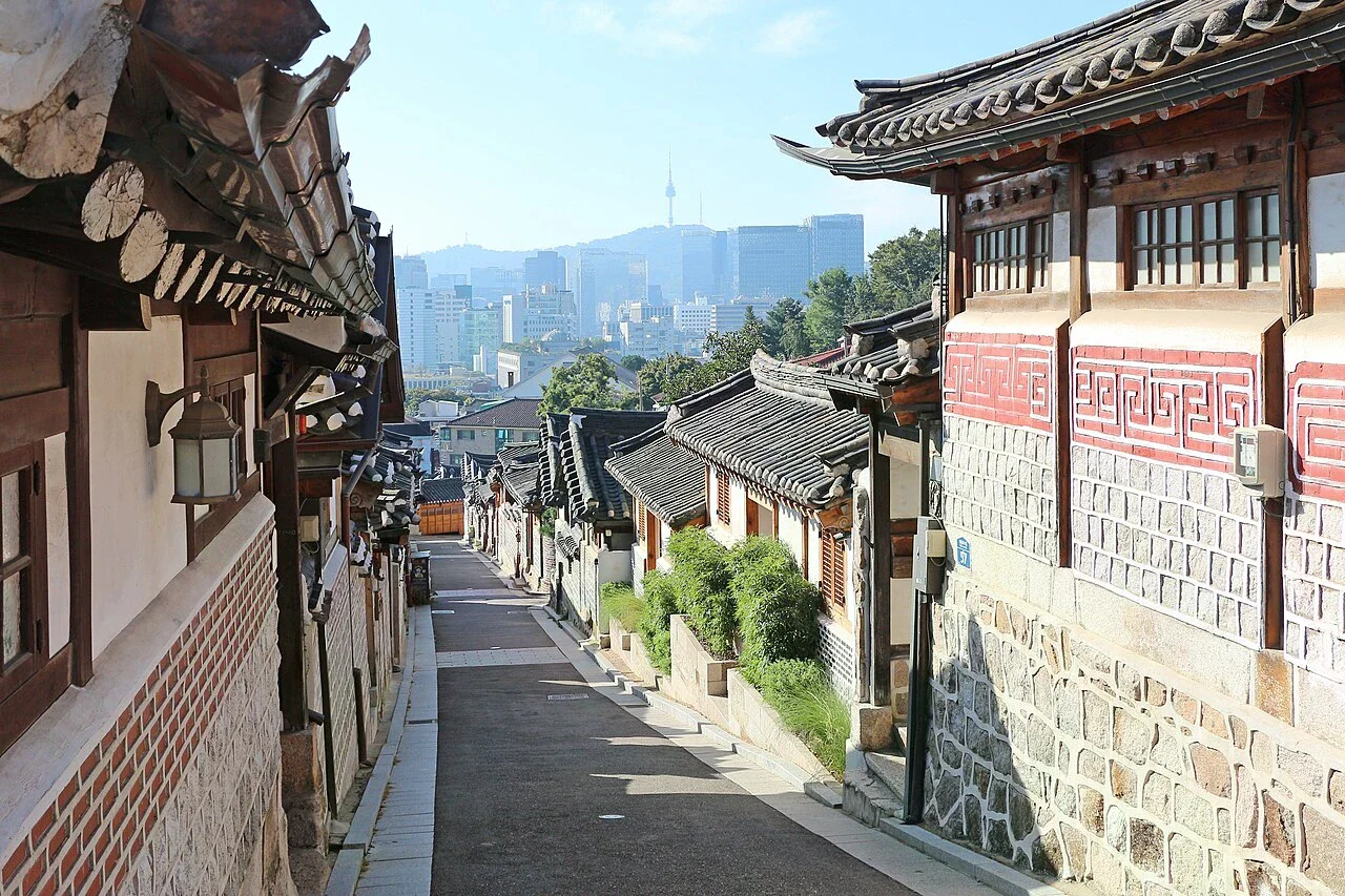北村韓屋村的一段巷道，兩側是傳統韓屋，遠方可見首爾市景