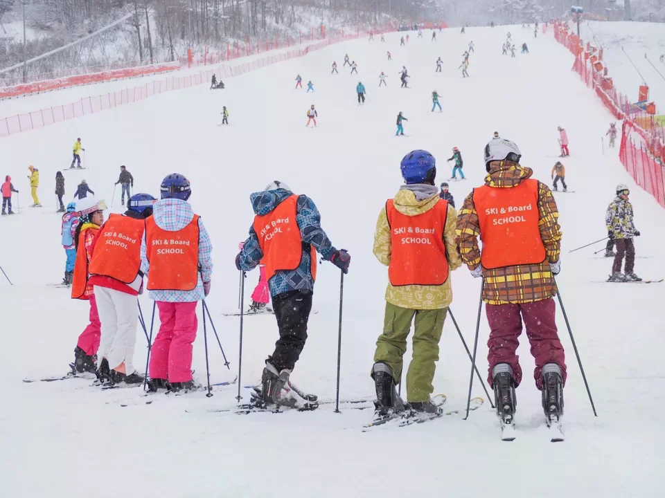 平昌滑雪場上多位學員穿紅色滑雪學校背心，在雪道上練習與聽教練說明