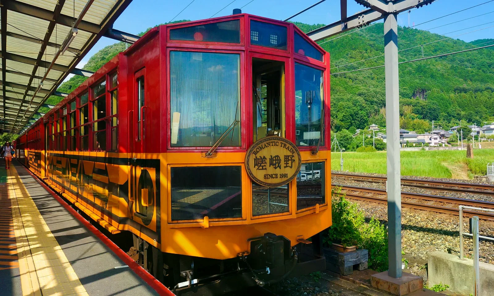 紅黃配色的浪漫小火車停靠月台，車頭有嵯峨野 ROMANTIC TRAIN 銘板