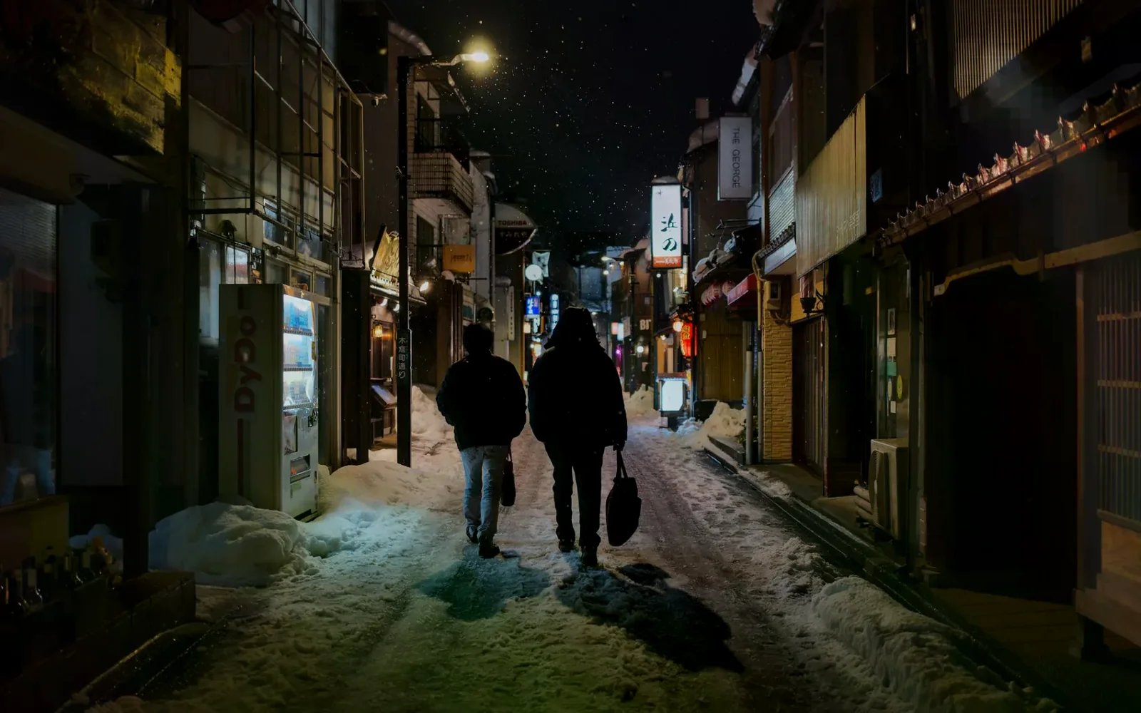 金澤夜間巷弄積雪，兩位行人沿著街道前進