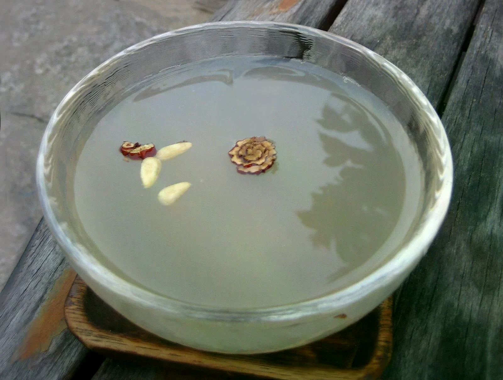 透明玻璃碗盛著淡乳白色的甜米露，表面飄著松子與切片紅棗，放在木桌上。
