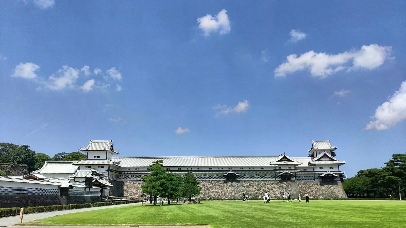 金澤城白色城牆上的長屋建築與石垣，前方有草地。