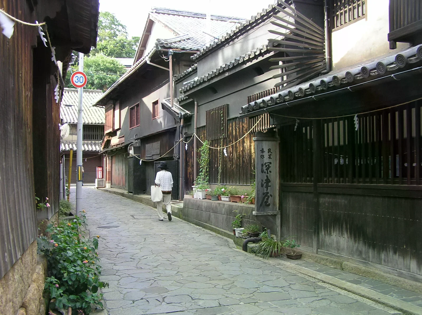 石板路穿過兩側木造町家，一位行人走在巷中