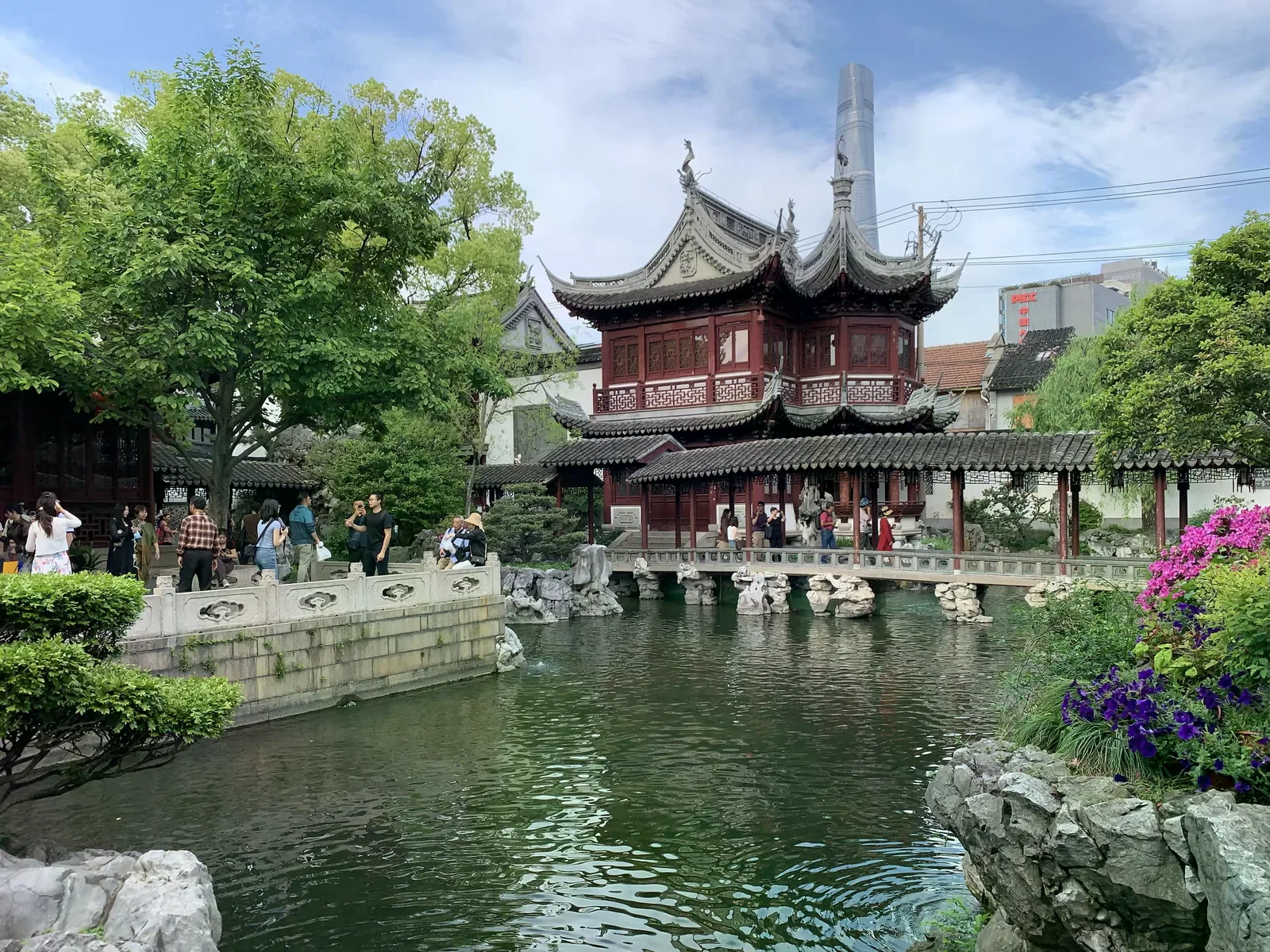 豫園內臨池而建的紅柱飛檐中式樓閣，池邊有遊客駐足，遠處天際線露出上海中心大廈。