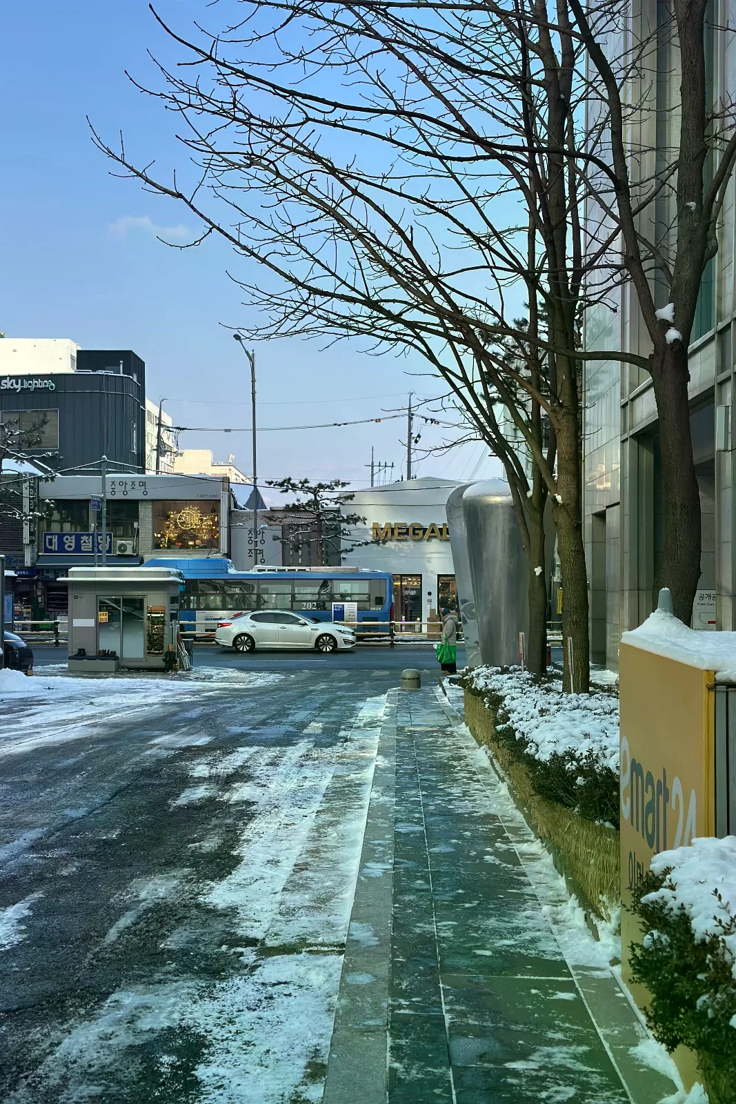 首爾街道人行道上的積雪與融雪，前方有車輛通行