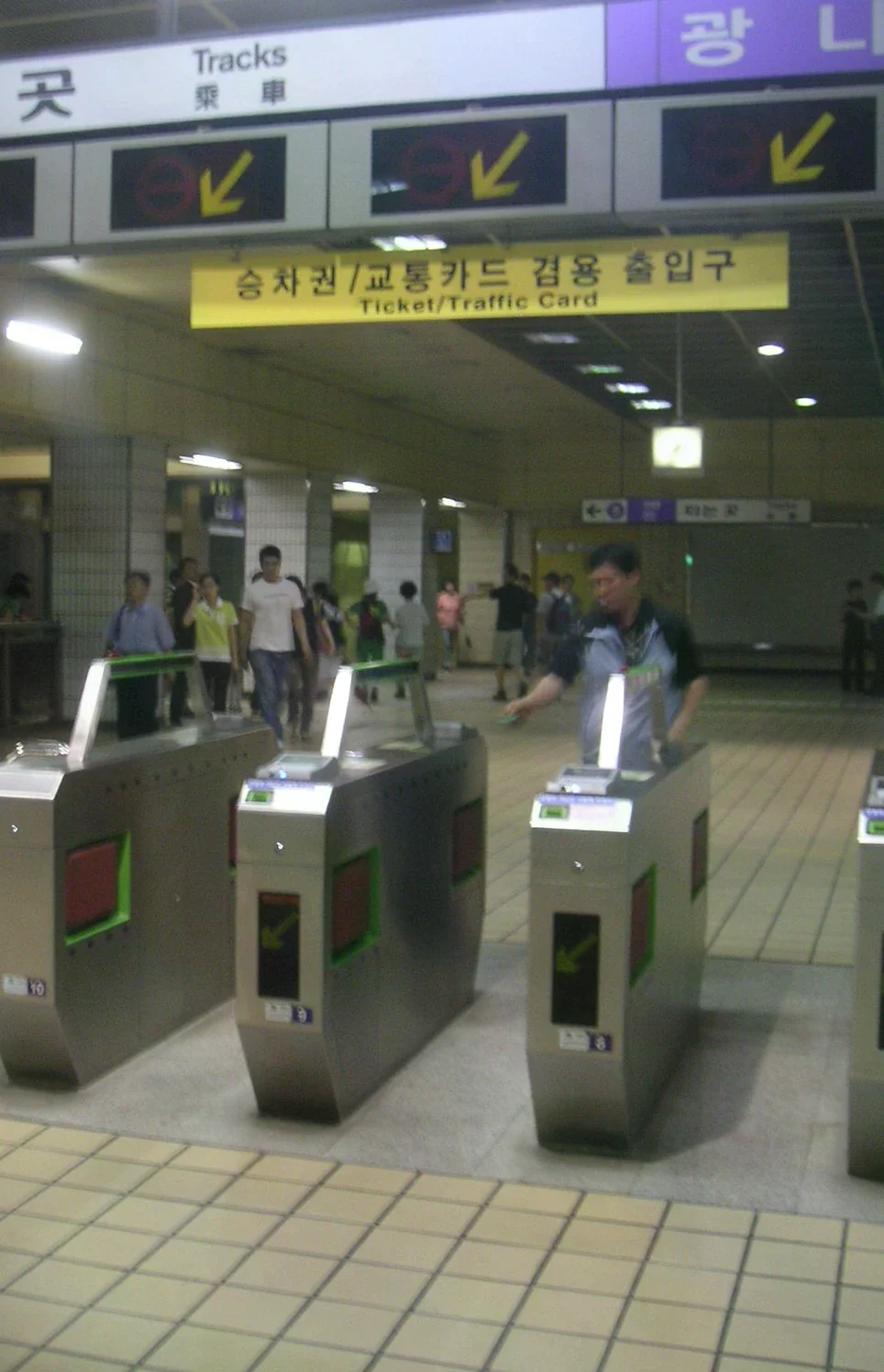首爾地鐵閘門旁有韓文與英文交通卡入口指示，乘客正在通過閘門