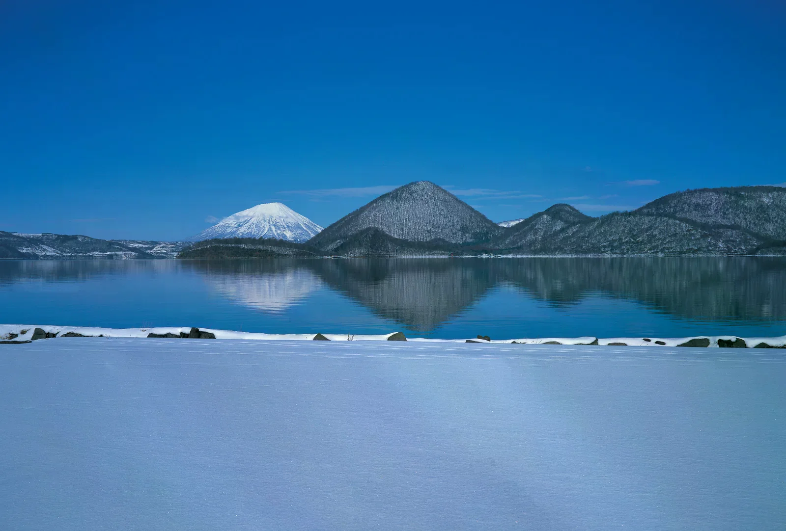 雪覆湖岸前的洞爺湖、山景與水面倒影