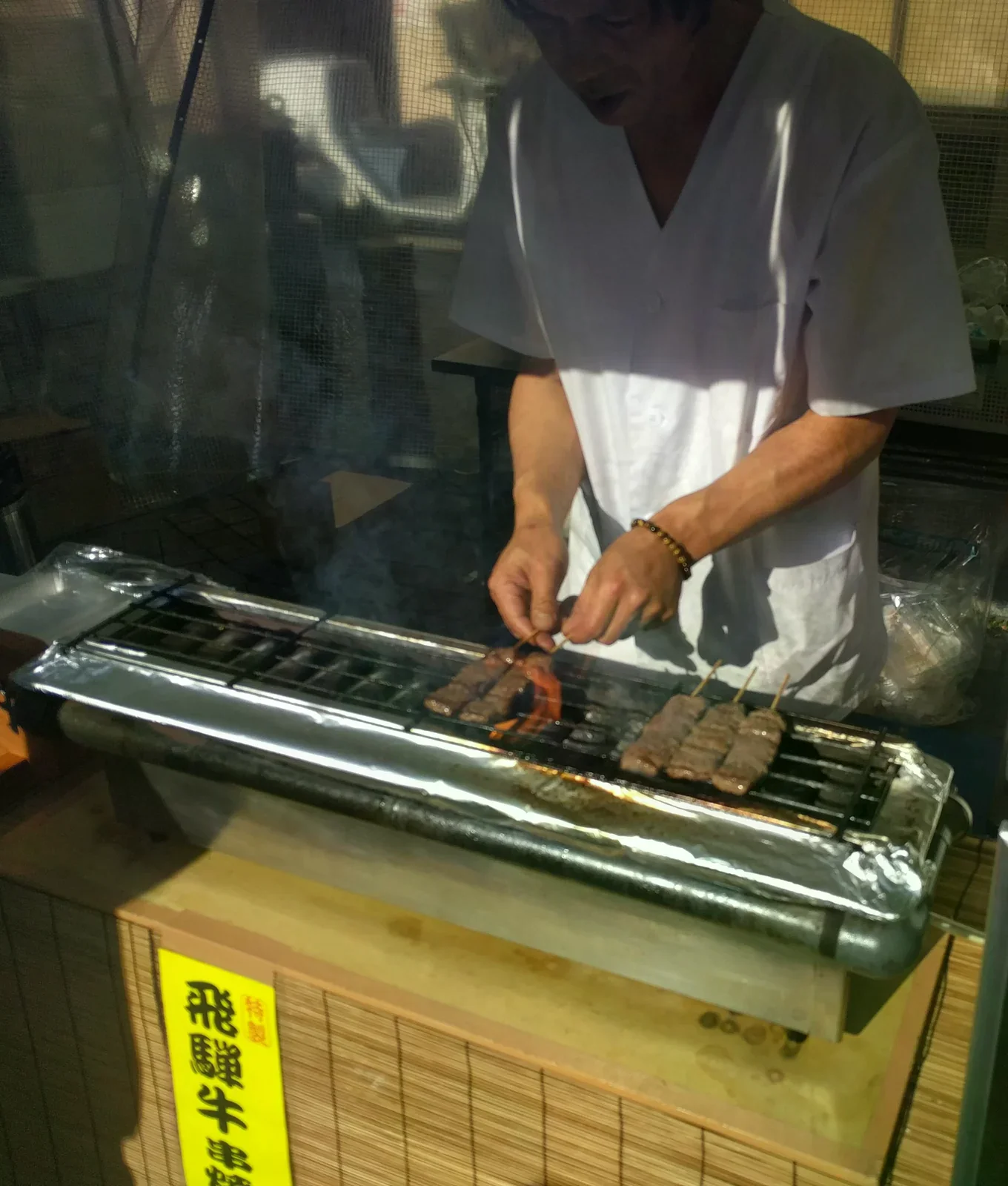 烤架上排著飛驒牛串，店員正在翻烤