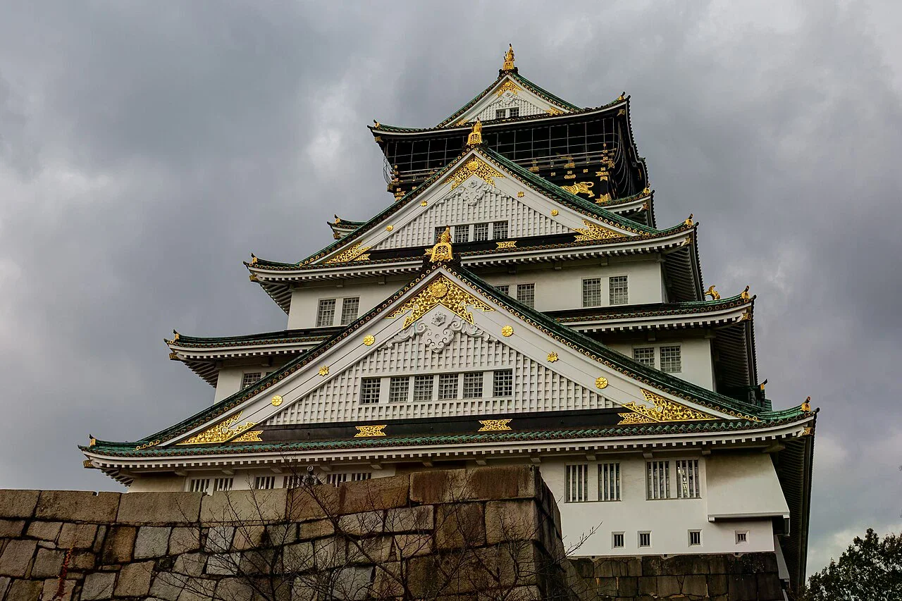 大阪城天守閣近景，畫面可見層疊屋頂、石垣與金色裝飾