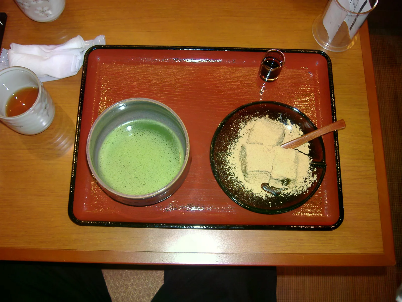 托盤上的抹茶與撒有黃豆粉的蕨餅，旁邊放著黑蜜
