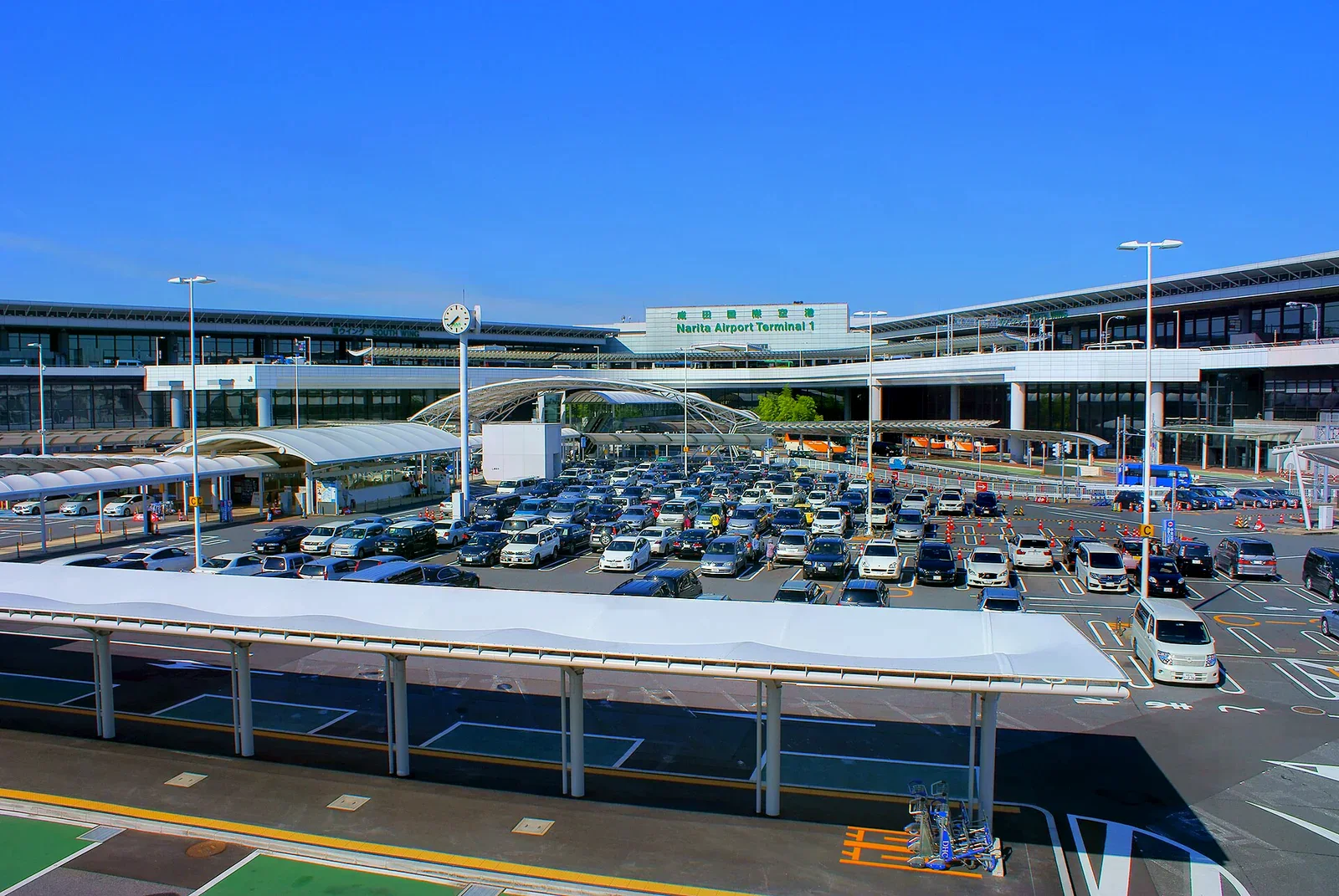 成田機場第一航廈外觀，前方是停車場與車道，建築上方有綠色 Narita Airport Terminal 1 字樣