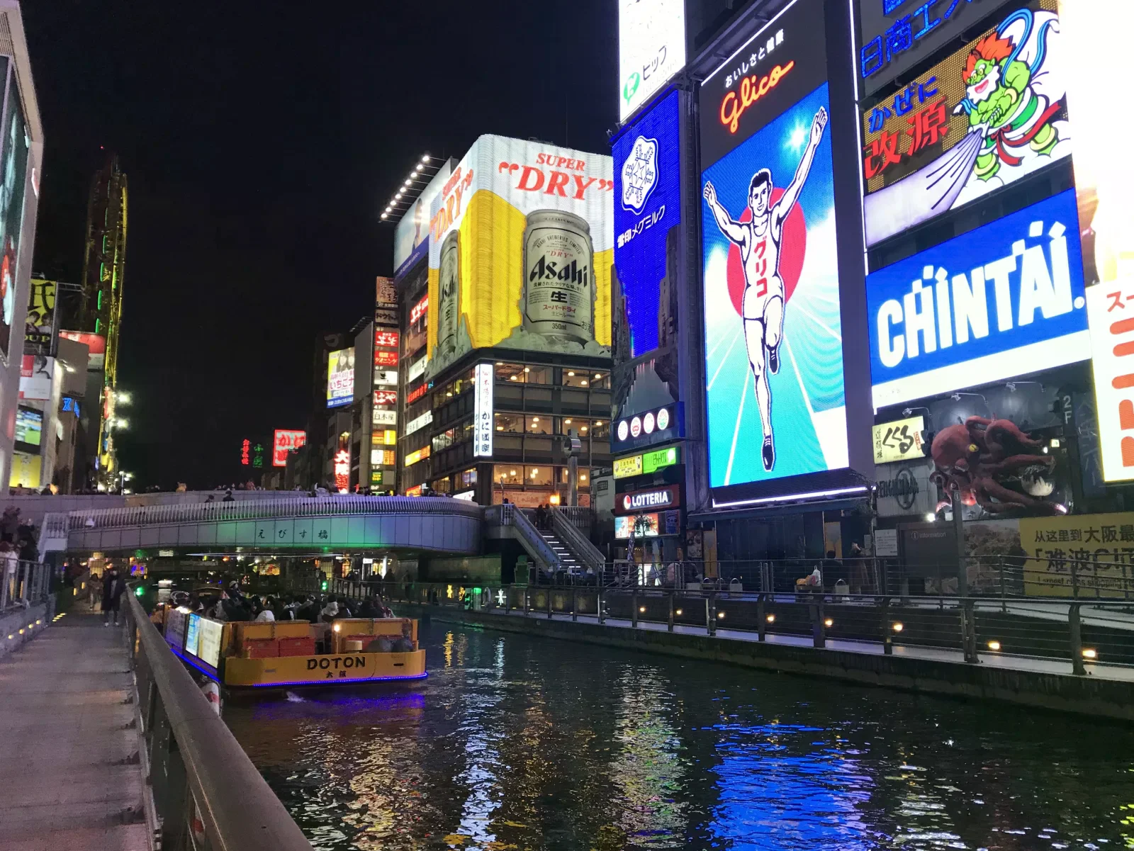 夜間道頓堀，格力高跑者霓虹招牌亮起，戎橋旁有水上觀光船停靠。