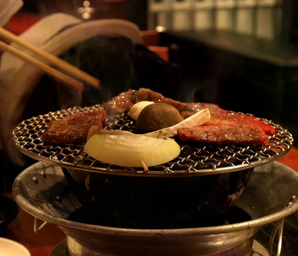 七輪烤網上肉片、洋蔥與香菇冒著熱煙，暖光照射