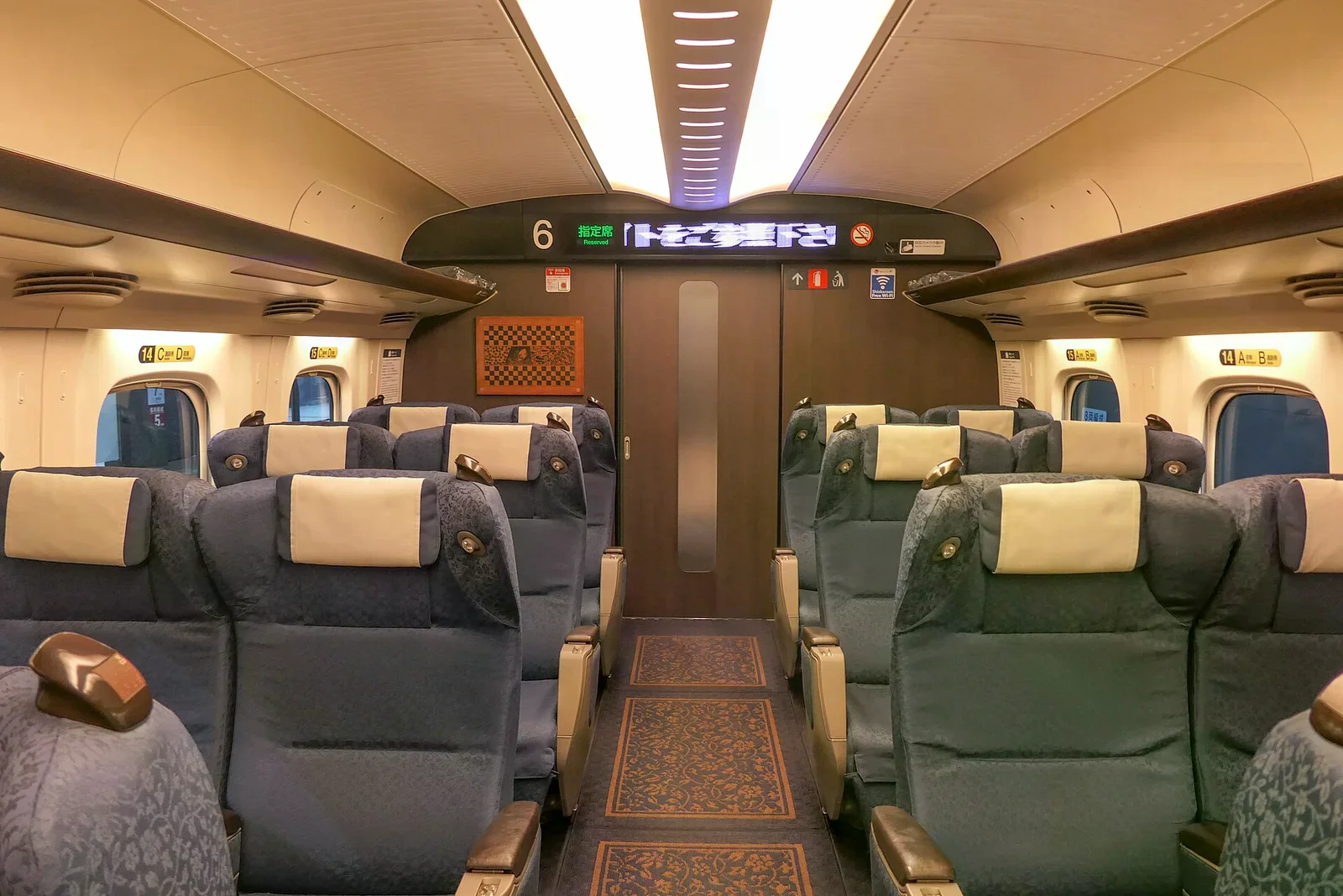 新幹線綠色車廂內部，藍色寬敞座椅成兩排配置，車尾有車號與指定席標示。