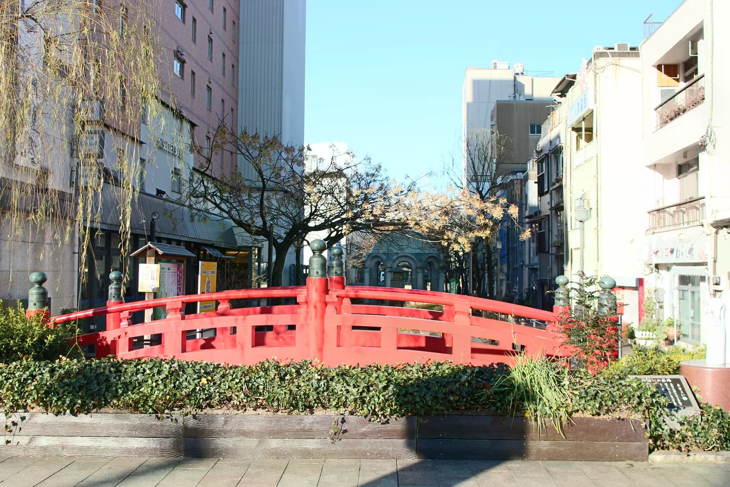市區綠地中的朱紅欄杆小橋，兩側是街屋與落葉樹