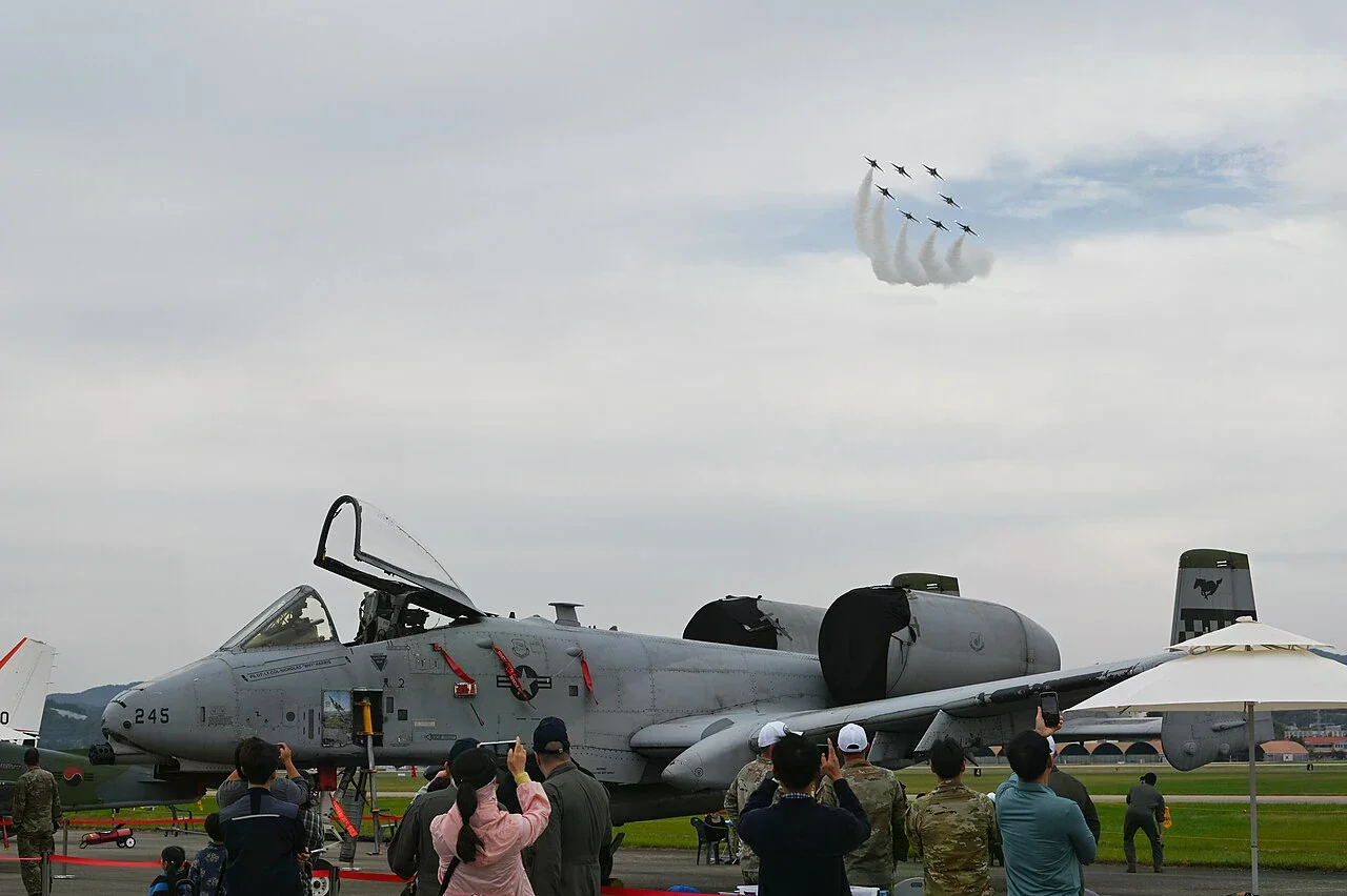 2024 年泗川航空展現場，A-10 靜態展示機前有觀眾，空中的黑鷹編隊正拉出煙跡