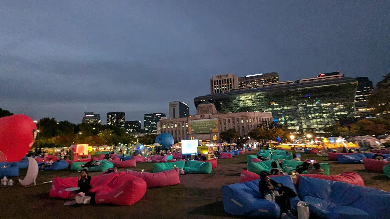首爾廣場戶外圖書館夜間場景，廣場上有彩色閱讀座椅與市政廳建築