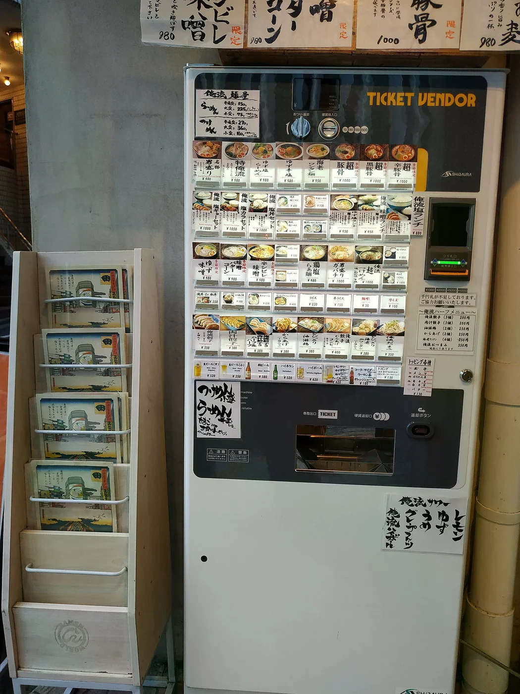 拉麵店門口的食券機，面板上排滿餐點照片、名稱與價格按鈕，標示著味噌、豚骨等品項與替玉價格