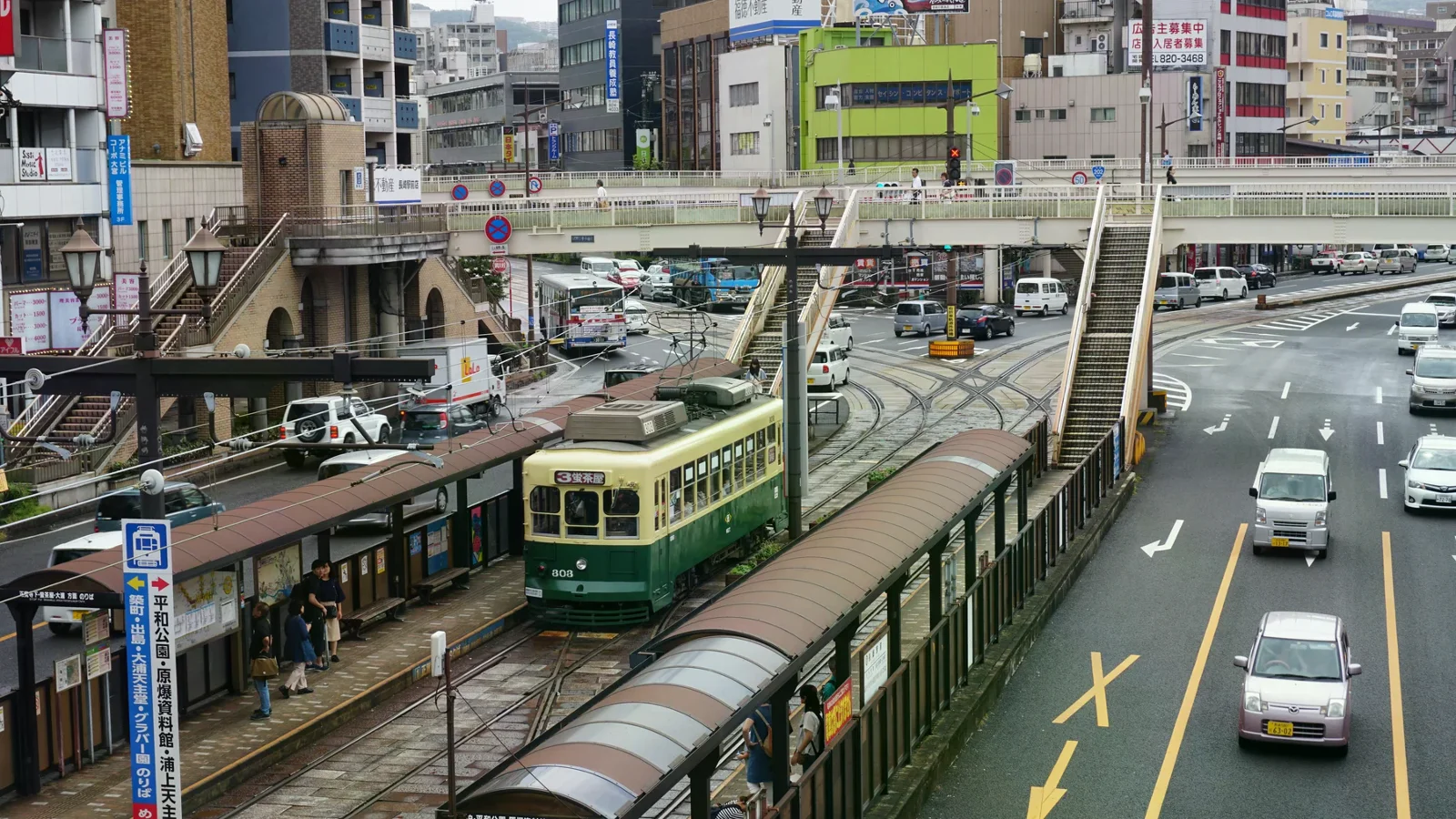 綠色路面電車沿街行駛，旁邊可見軌道與人行天橋