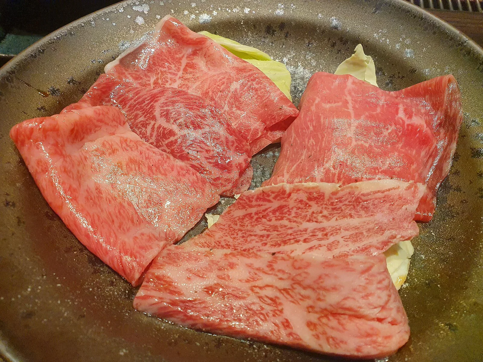 深色盤上的霜降生牛肉薄片鋪在高麗菜上