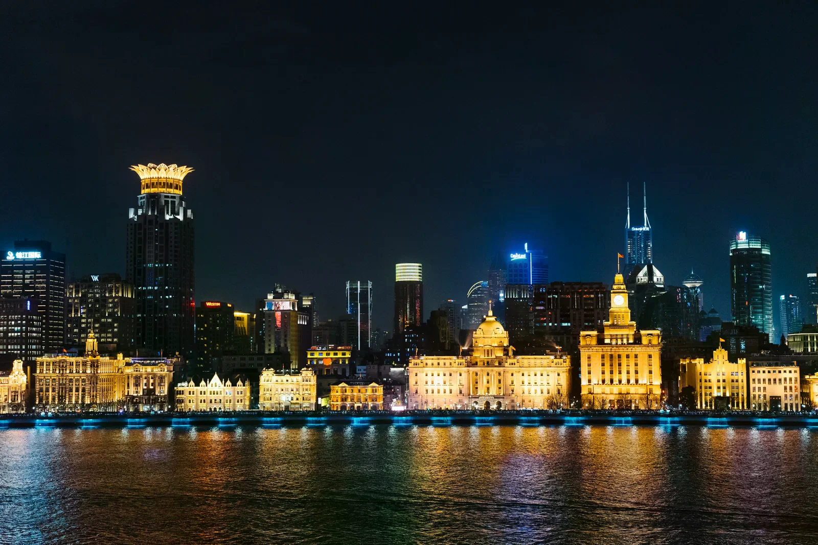 入夜後黃浦江畔外灘歷史建築群點燈，海關大樓鐘樓與圓頂銀行建築倒影落在江面。