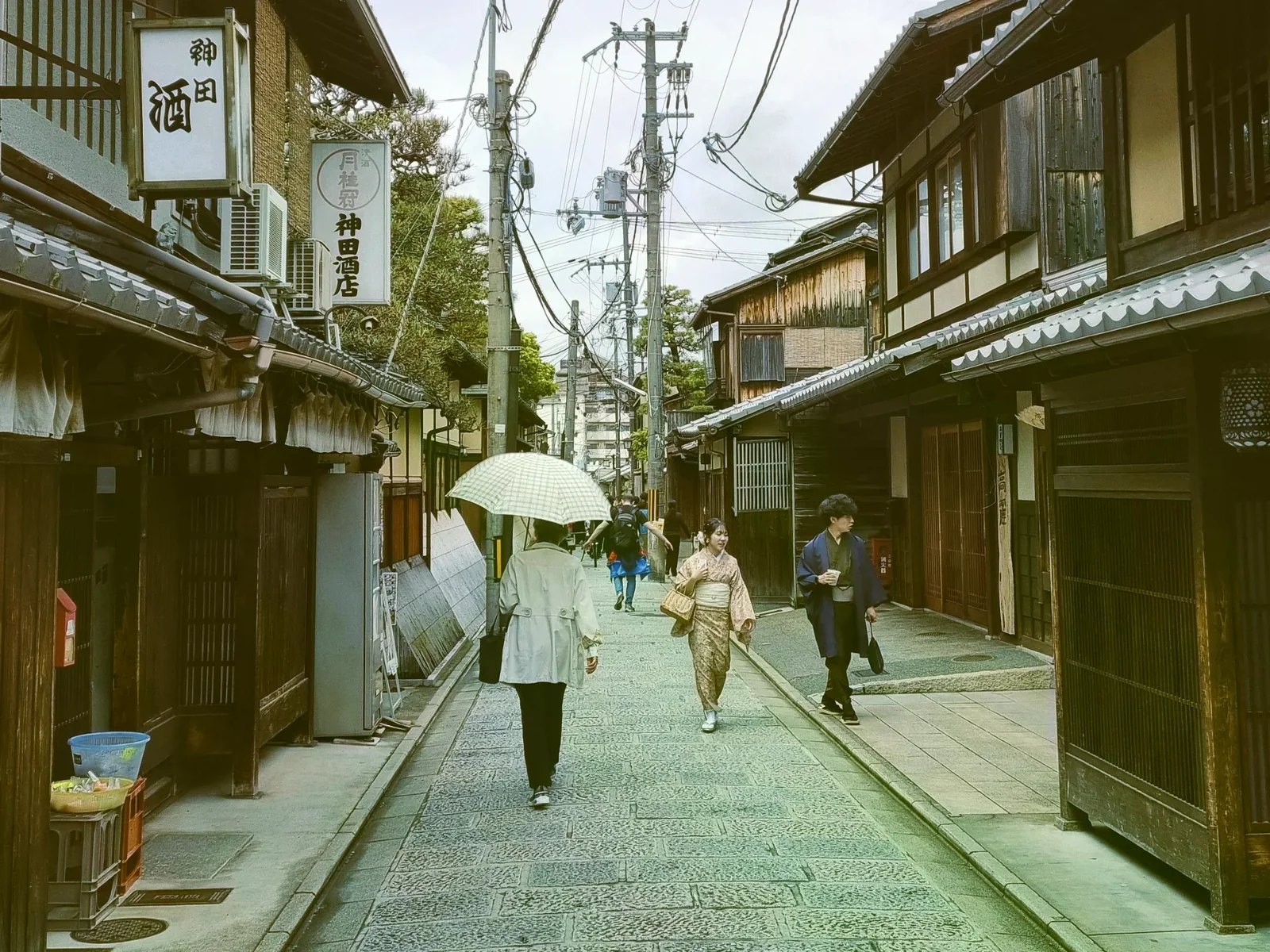 京都傳統街道上，幾位行人撐著雨傘走在木造街屋之間