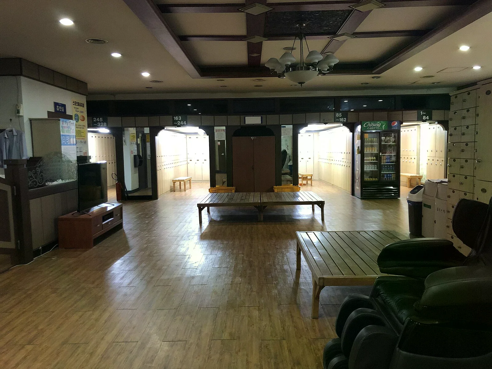 汗蒸幕休息大廳，木質地板上擺著長形木平台與黑色躺椅，後方依編號區分出多間置物櫃入口，旁邊有飲料販賣櫃。