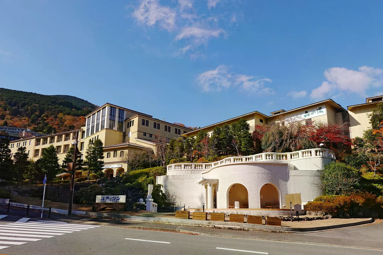 山坡上的日歸溫泉設施建築群，外牆設有設施招牌與白色拱廊